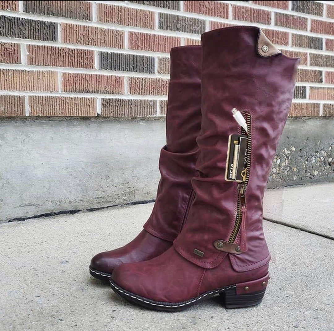Burgundy leather knee-high boots with side zipper pocket holding cards and USB drive on concrete