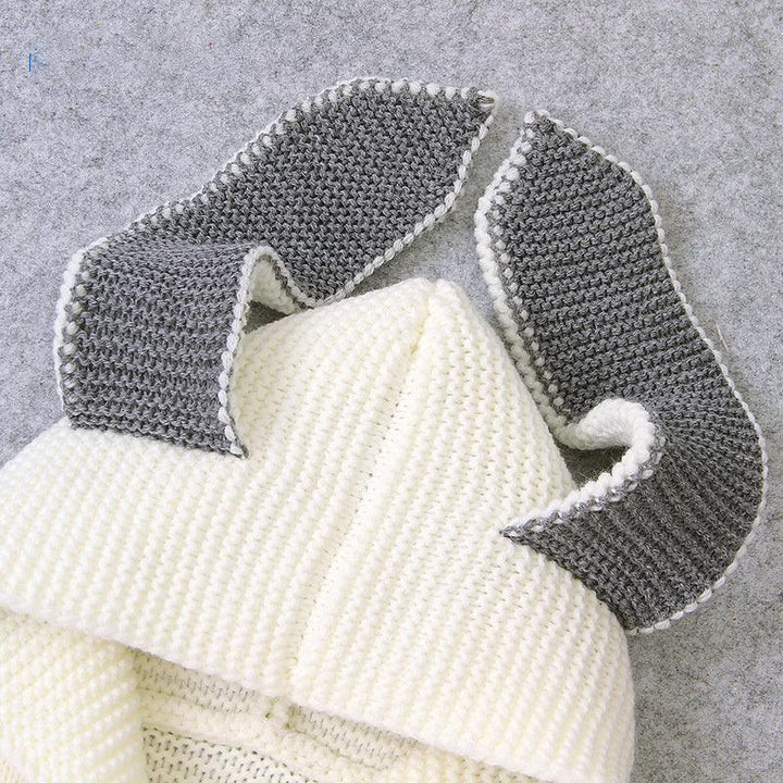 Handmade white knitted bunny hat with long gray ears on gray background