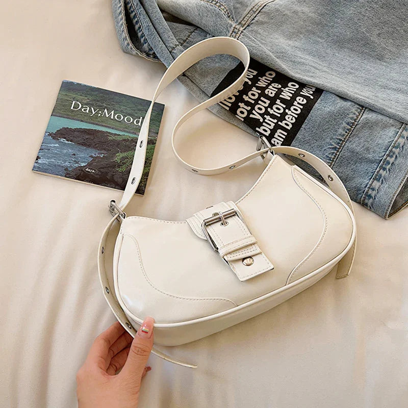 White leather shoulder bag with buckle detail beside denim jacket and Day Mood booklet on beige surface