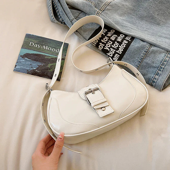 White leather shoulder bag with buckle detail beside denim jacket and Day Mood booklet on beige surface