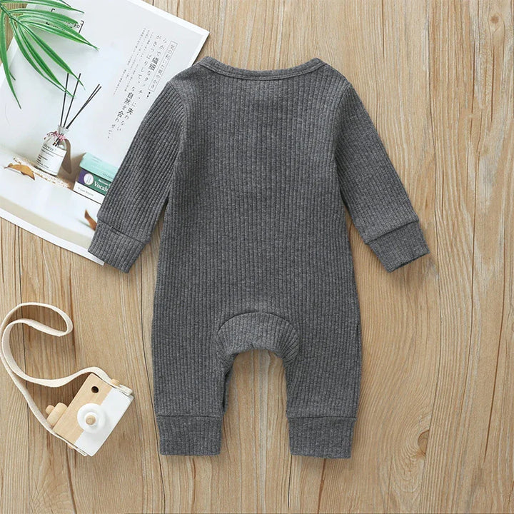 Gray ribbed baby onesie with long sleeves on wooden surface, styled with magazine and toy camera