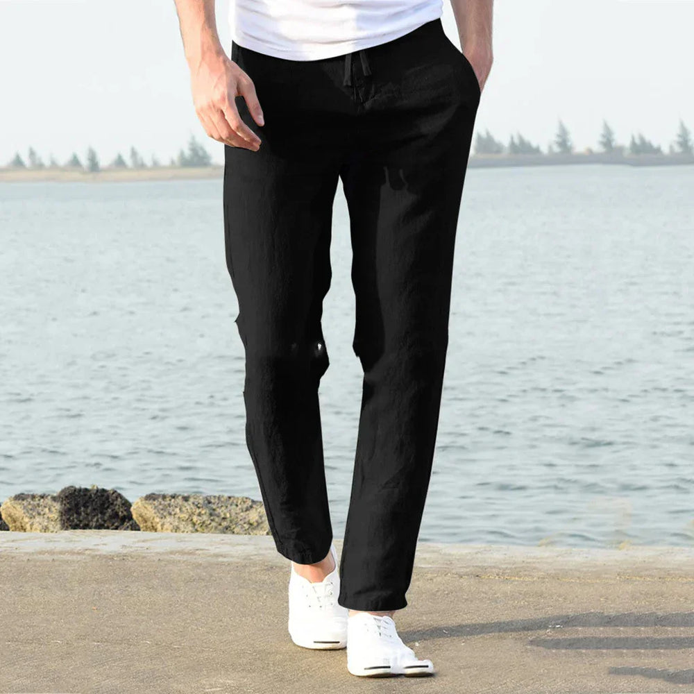 Man wearing black casual pants and white sneakers walking on seaside pavement