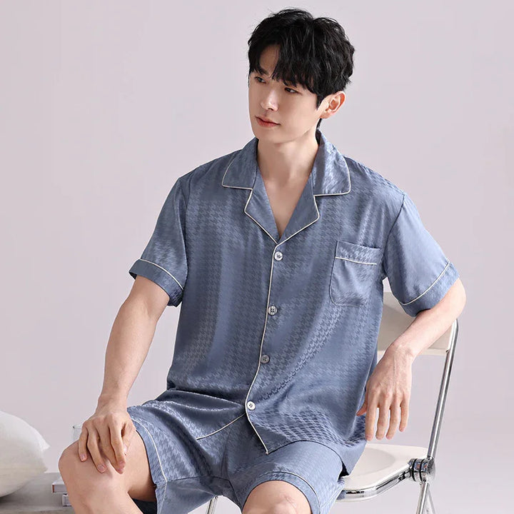 young man wearing light blue satin short sleeve pajama set sitting on white chair