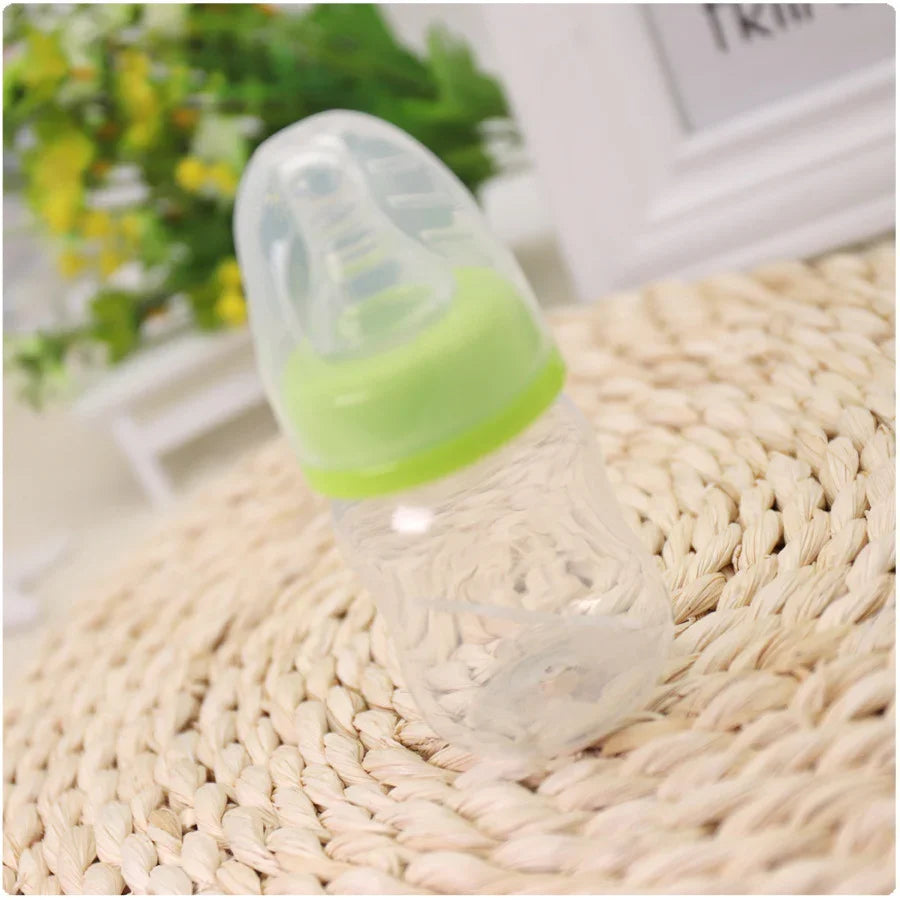 Clear baby bottle with green cap on woven surface with blurred green plants in background