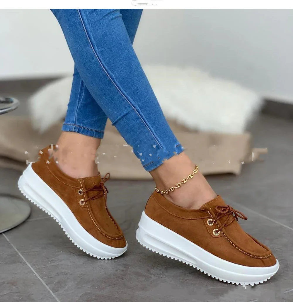 Brown suede platform sneakers with white thick soles worn with blue skinny jeans and gold anklet indoors
