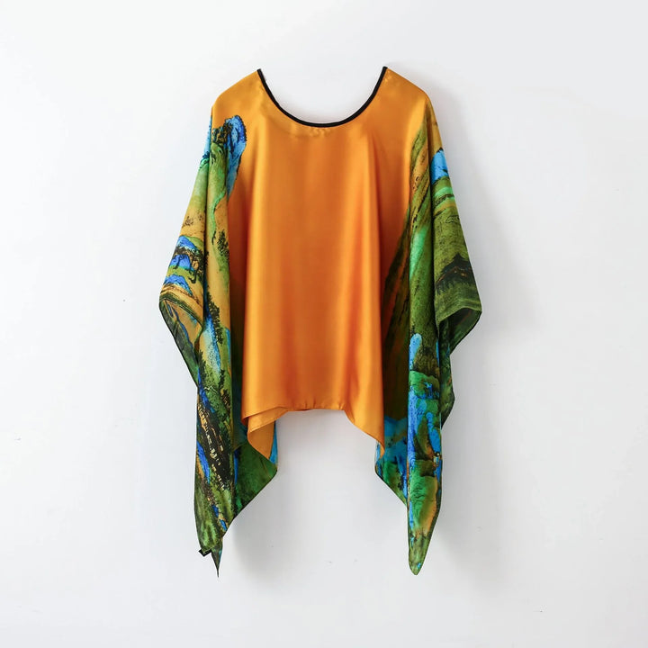 Silk kaftan with vibrant orange center and blue-green landscape print sleeves hanging on white wall