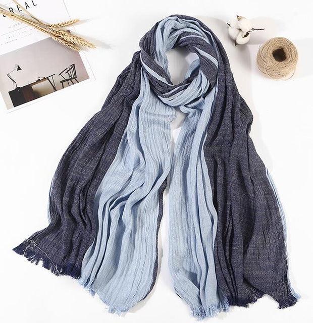 Light blue and dark blue striped cotton scarf laid out with stationery, wheat stalks, cotton flower, and twine on white surface