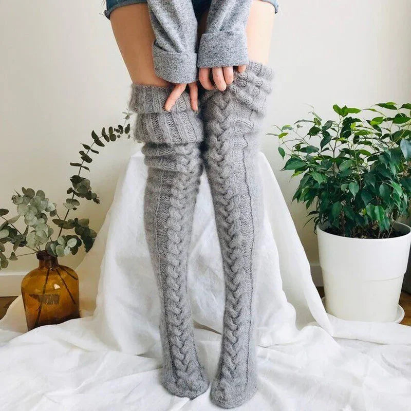 Person wearing cozy gray cable knit thigh-high socks sitting with plants in the background