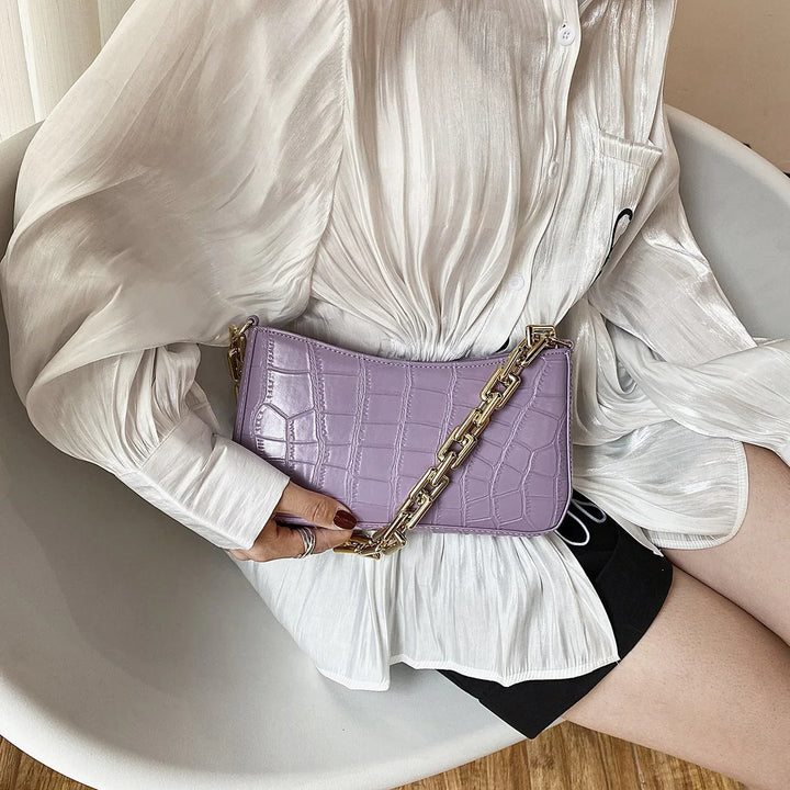 Woman wearing white silk blouse and black shorts holding lavender crocodile leather handbag with gold chain