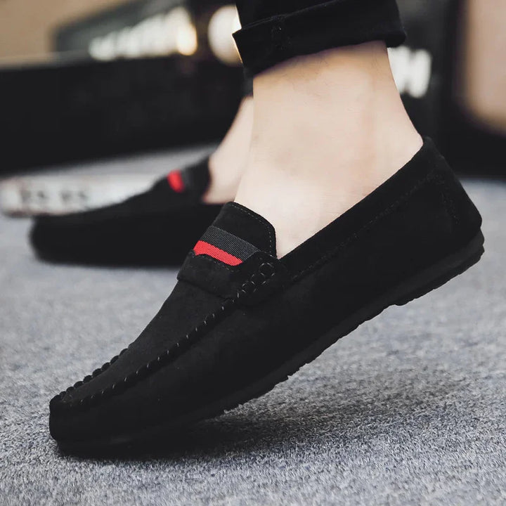 Close-up of black suede moccasin loafers with red and black fabric detail worn on feet