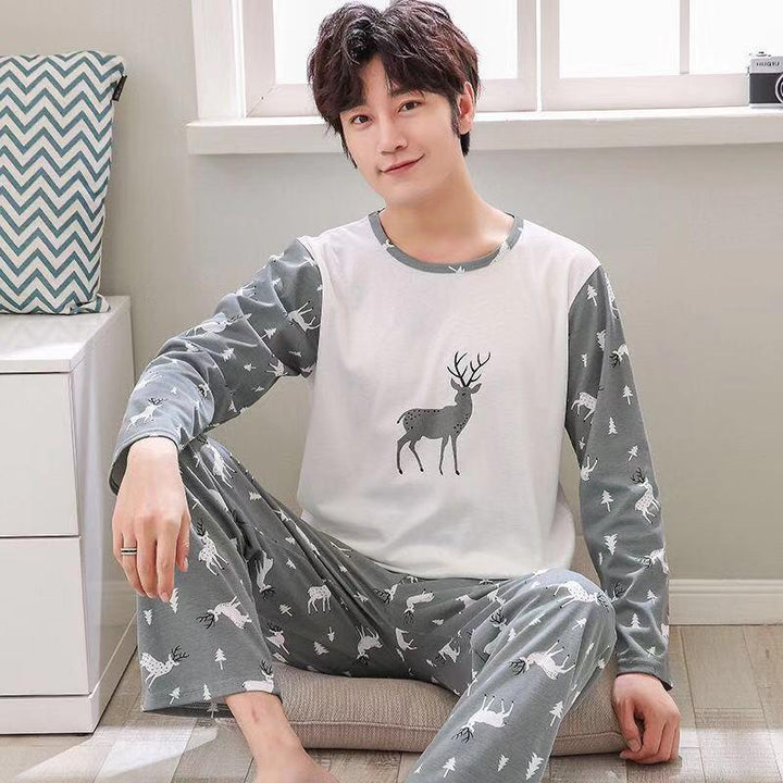 Smiling young man wearing grey and white deer print pajamas sitting on cushion in cozy room