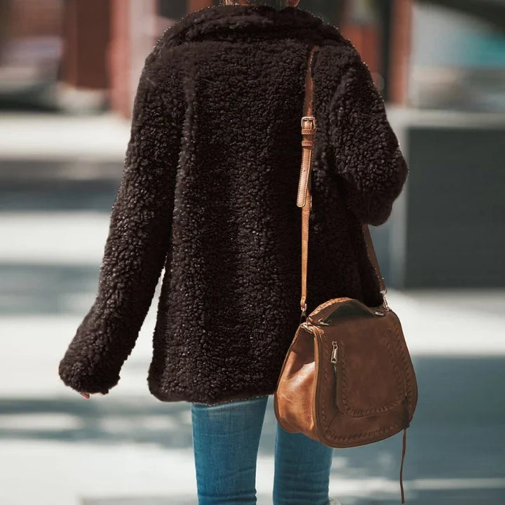 Person wearing a dark brown sherpa jacket and blue jeans carrying a vintage brown leather handbag outdoors