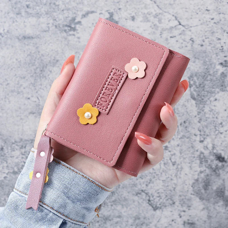 Hand holding a pink leather wallet decorated with yellow and pink flower appliques against a gray textured background