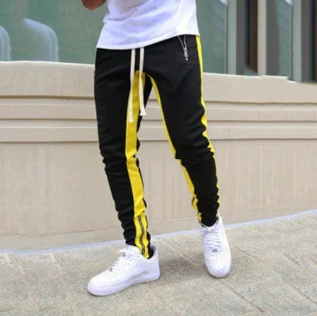 Man wearing black jogger pants with yellow stripes and white sneakers outdoors