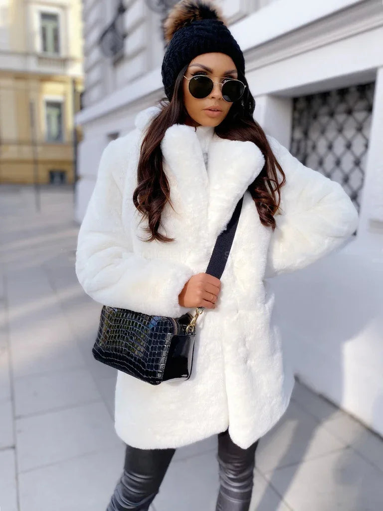 Woman wearing white faux fur coat, black leather pants, black pom-pom beanie, sunglasses, and black textured handbag outdoors