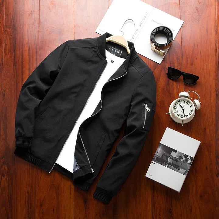 Black bomber jacket with white inner shirt on wooden surface with belt, sunglasses, clock, and magazine