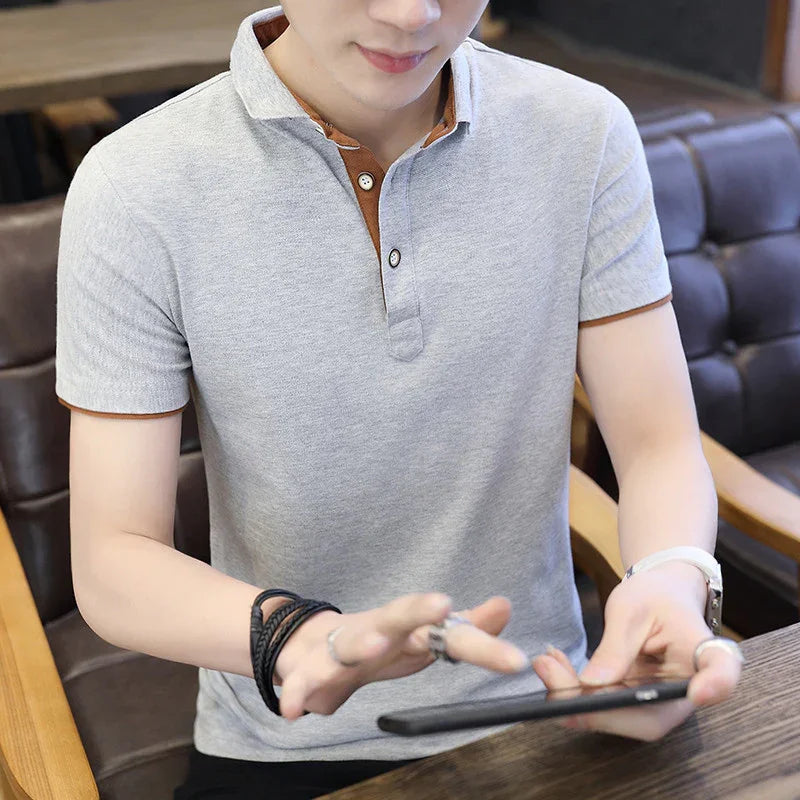 Man wearing gray polo shirt with brown collar details using smartphone at wooden table in cafe