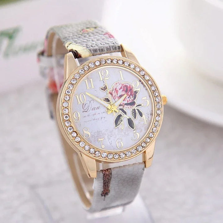 Elegant gold-tone wristwatch with rhinestone bezel, floral dial design, and patterned gray leather strap