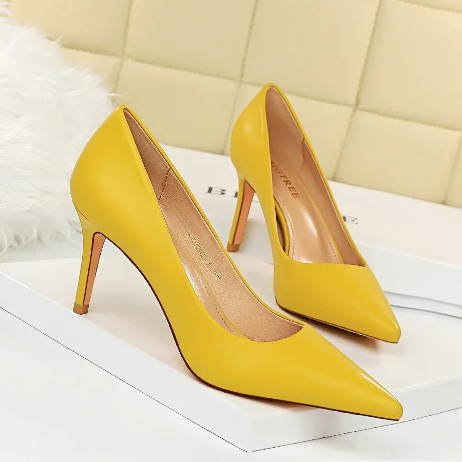 Pair of yellow pointed-toe high heel pumps on a white surface with beige quilted background