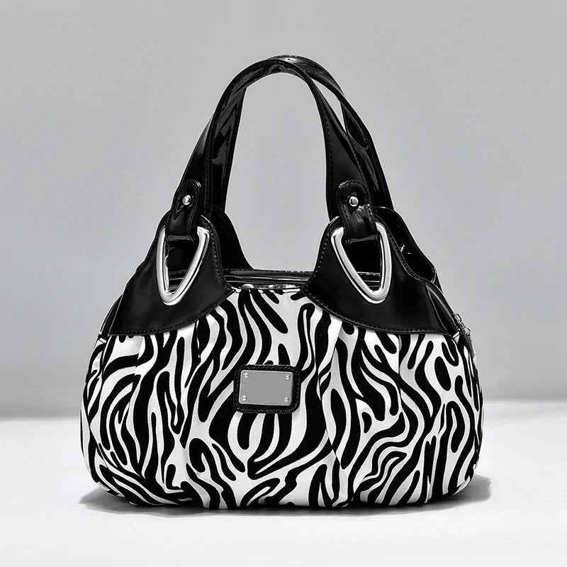 Black and white zebra print handbag with black patent leather handles and silver hardware on gray background