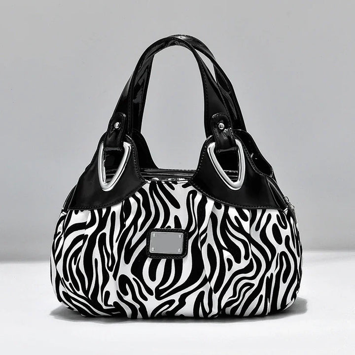 Black and white zebra print handbag with black patent leather handles and silver hardware on gray background