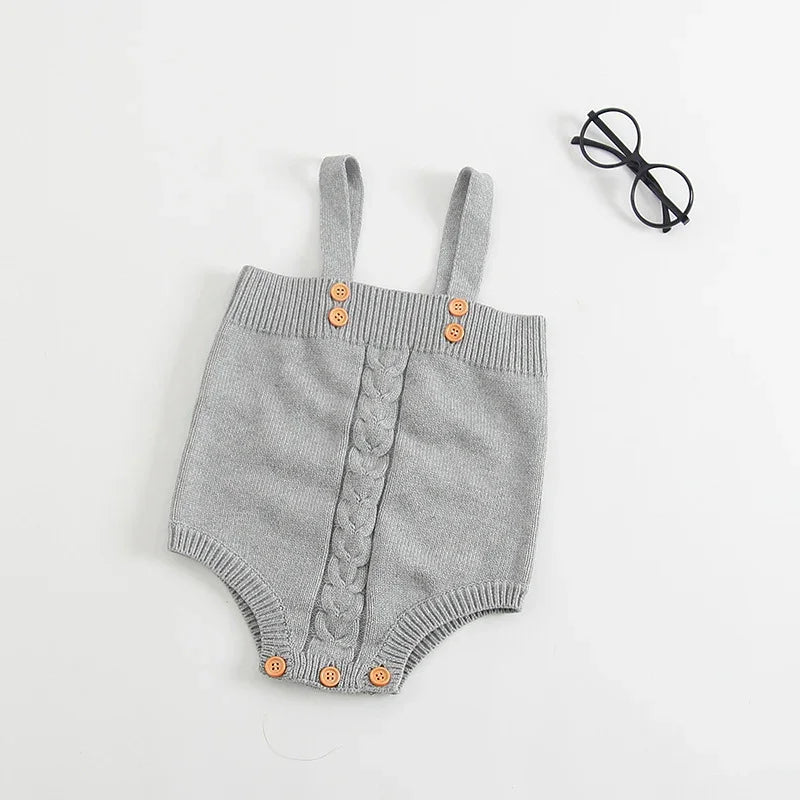 Gray knitted baby romper with straps and wooden buttons laid flat on white background with black round glasses