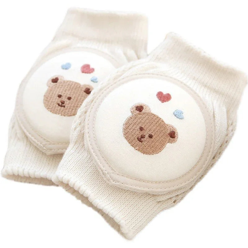Soft beige baby knee pads with embroidered teddy bear faces and heart accents