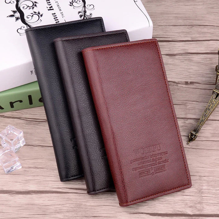 Three leather long wallets in brown, dark brown, and black on wooden surface with decorative book and Eiffel Tower model