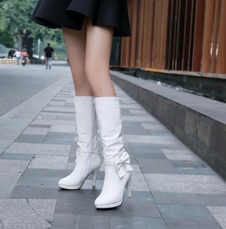 Woman wearing white high-heeled knee boots with bow detail on city sidewalk