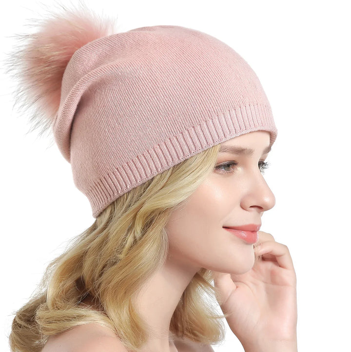 Side profile of a woman wearing a light pink knit beanie with a fluffy pom-pom