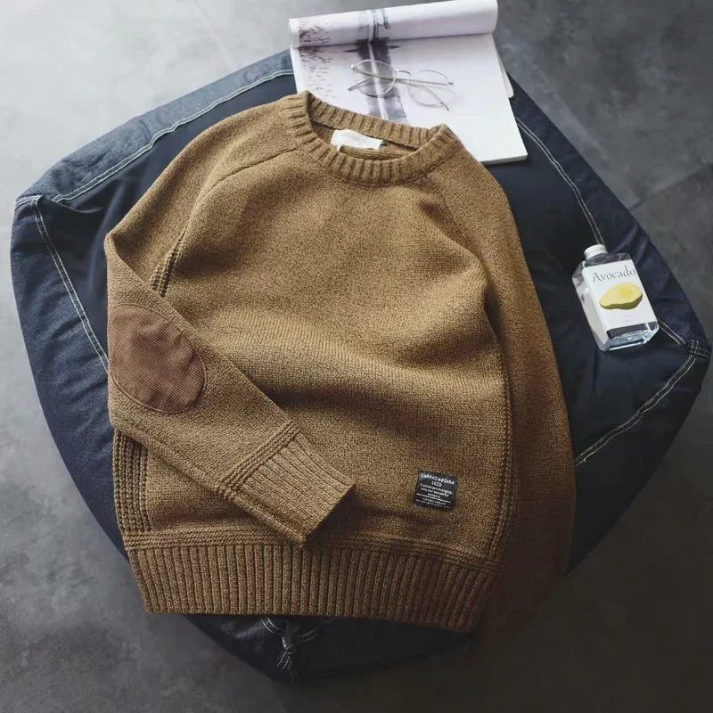 Brown knit sweater with elbow patches on black cushion, open book and small avocado water bottle