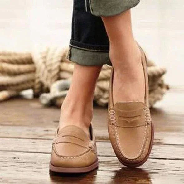 Close-up of casual tan leather loafers worn with cuffed jeans on wooden floor