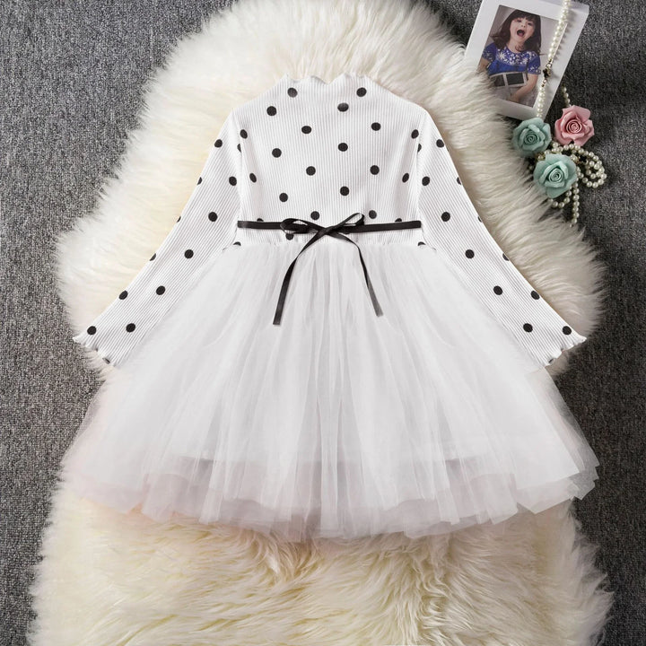 White child dress with black polka dot top and layered tulle skirt on fur rug, decorative flowers and photo