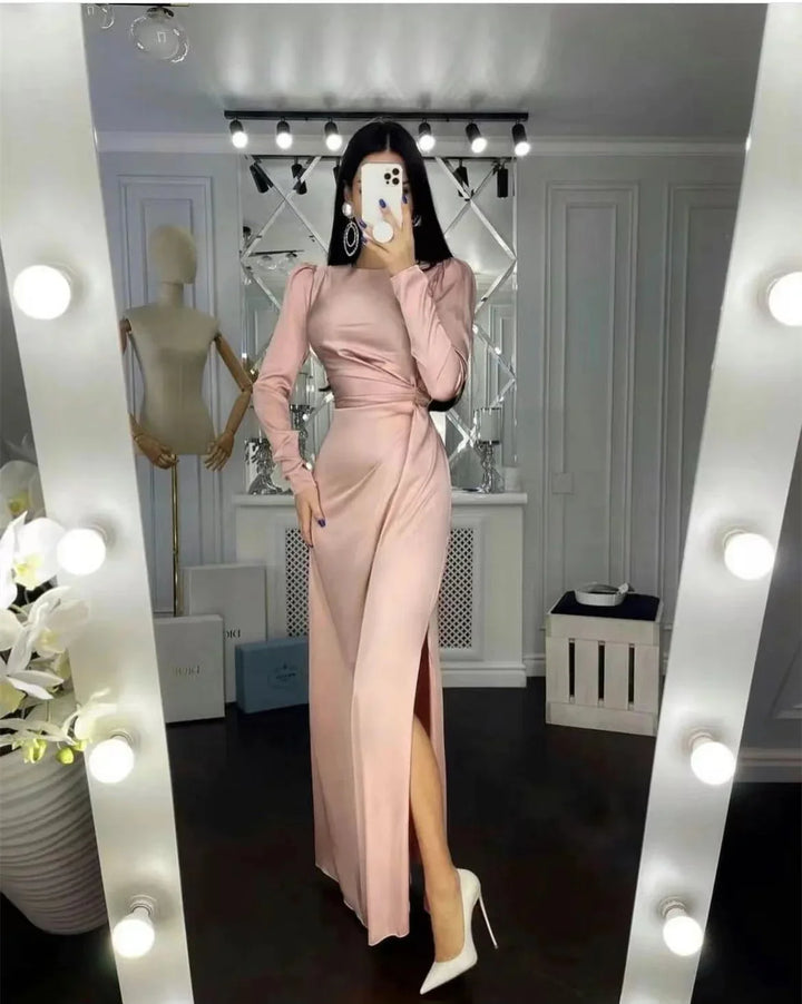 Woman in a long pink satin dress with side slit and white heels taking a mirror selfie in a stylish room