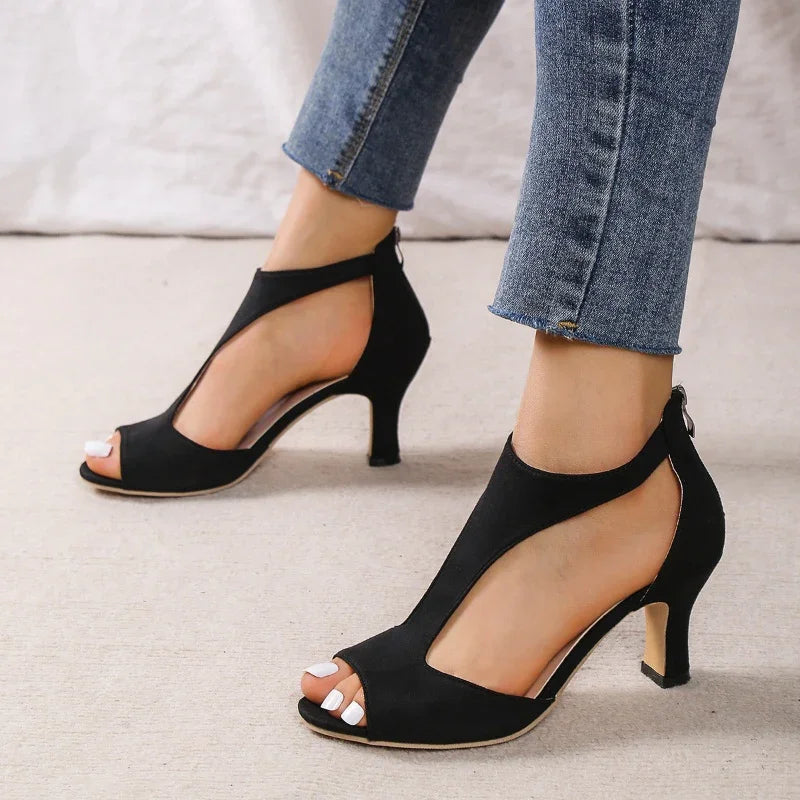 Close-up of woman's feet wearing black peep-toe high heels with zipper back, paired with blue skinny jeans