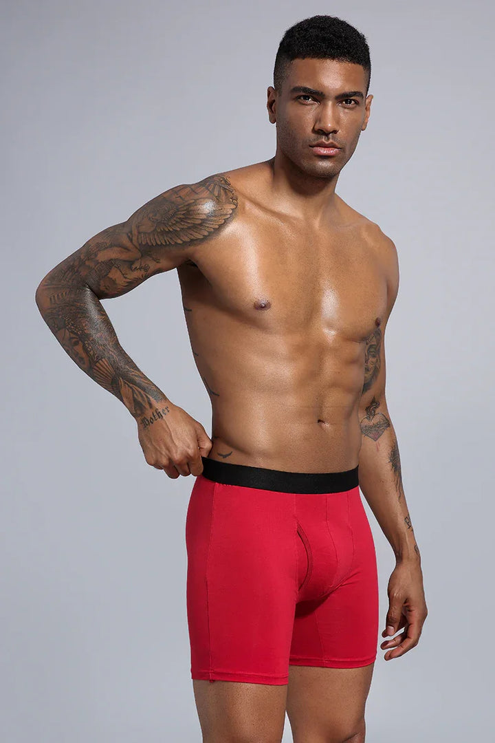 Shirtless man with tattoos wearing red boxer briefs with black waistband on gray background
