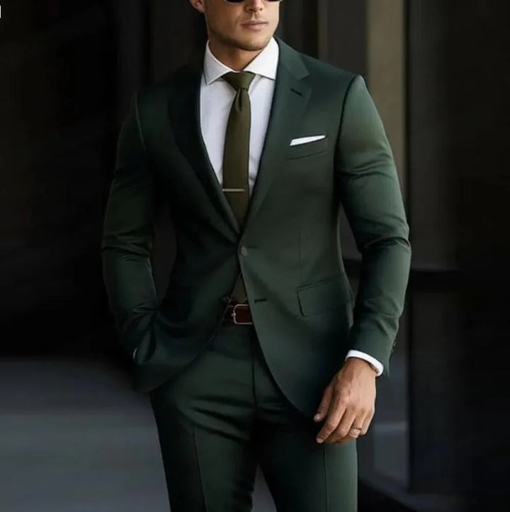 Man wearing a dark green slim-fit suit with white dress shirt, green tie, pocket square, and sunglasses