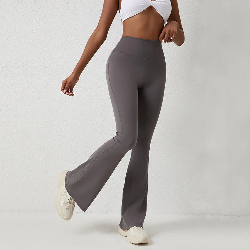 Woman wearing gray high-waisted flare leggings and white crop top against a white wall