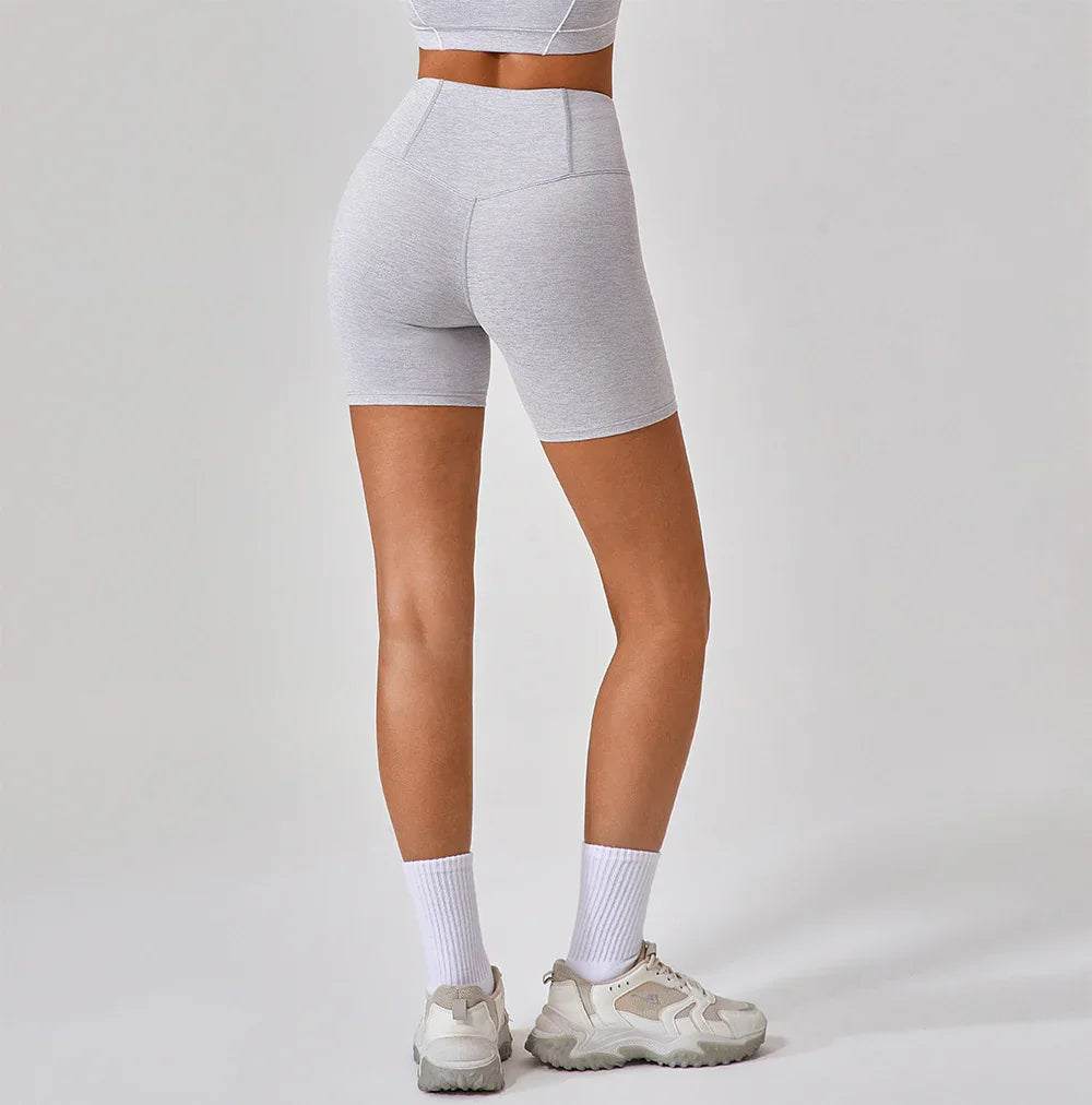 Back view of woman wearing light gray high-waisted biker shorts with white athletic socks and sneakers