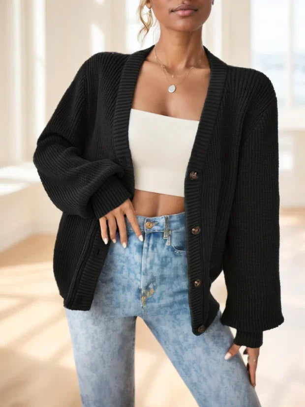 Woman wearing black oversized knit cardigan over white crop top and high-waisted light blue jeans in bright room