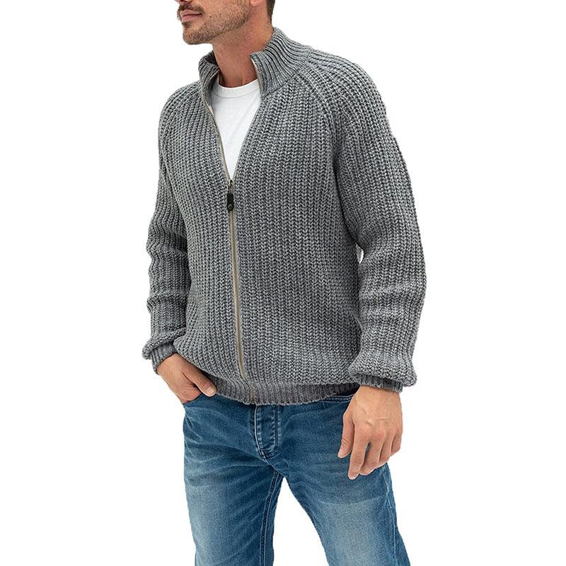 Man wearing grey knitted zip-up sweater and blue jeans on white background