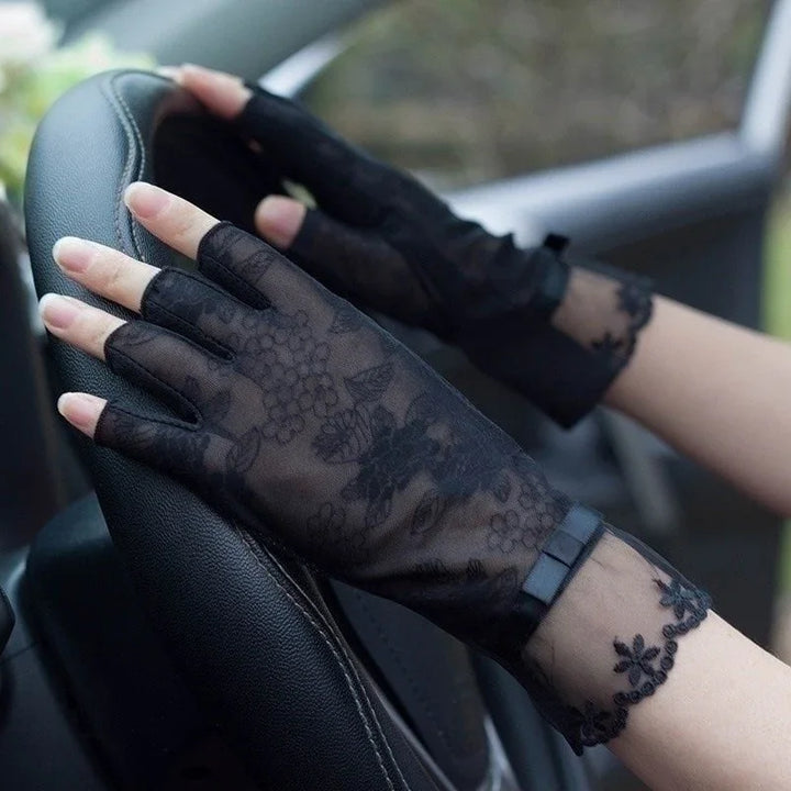 Hands wearing black lace fingerless gloves with floral patterns on a car steering wheel