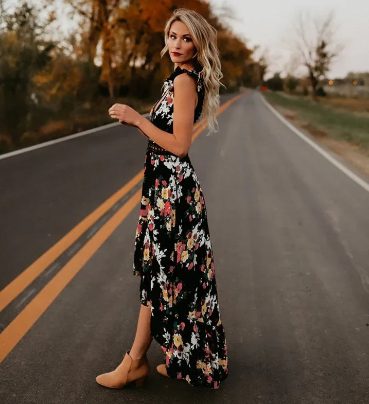 Blonde woman in a black floral maxi dress and tan ankle boots standing on a rural road with autumn trees