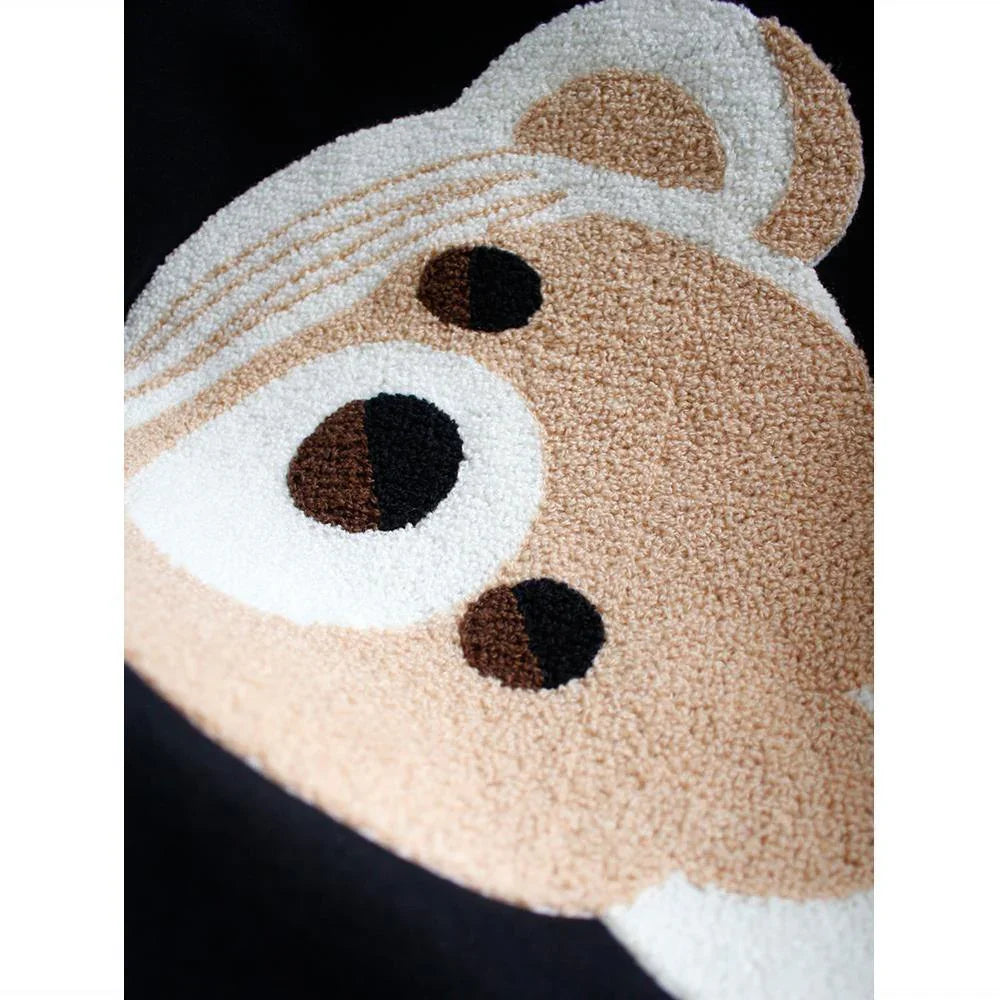 Close-up of embroidered teddy bear face with beige, white, and black threads on black fabric