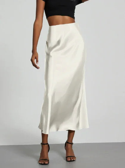 Woman wearing a white satin midi skirt with a black crop top and black high-heeled sandals