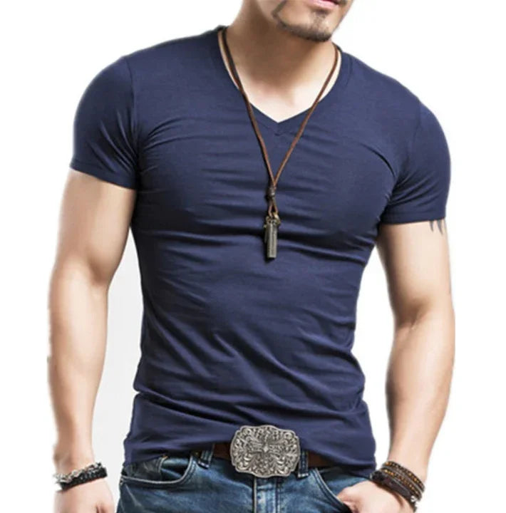 muscular man wearing navy blue V-neck fitted T-shirt, leather necklace, patterned belt buckle, and jeans
