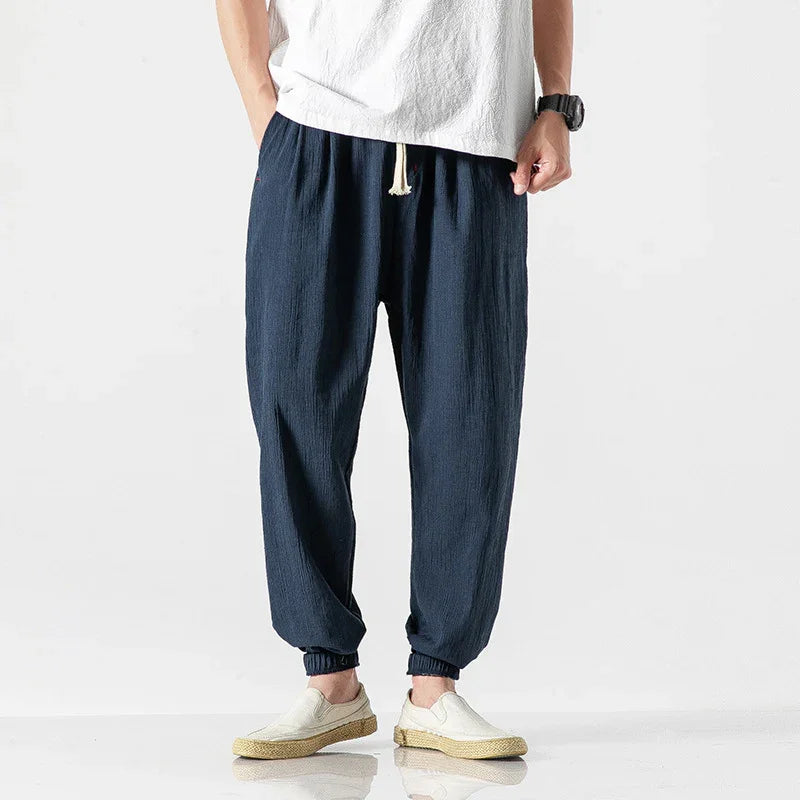 Men's casual navy blue linen jogger pants with elastic cuffs and white drawstring, paired with white slip-on shoes