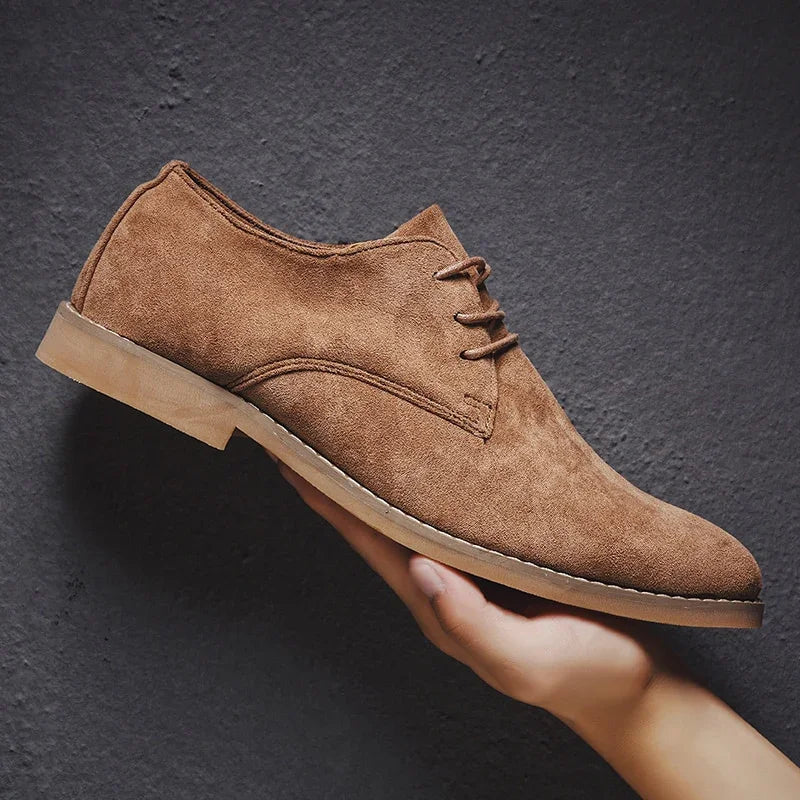 Hand holding a brown suede lace-up men's dress shoe on dark textured background