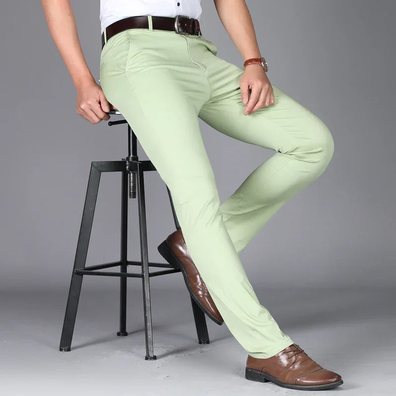 Man wearing light green slim-fit trousers with brown belt and brown dress shoes sitting on black metal stool