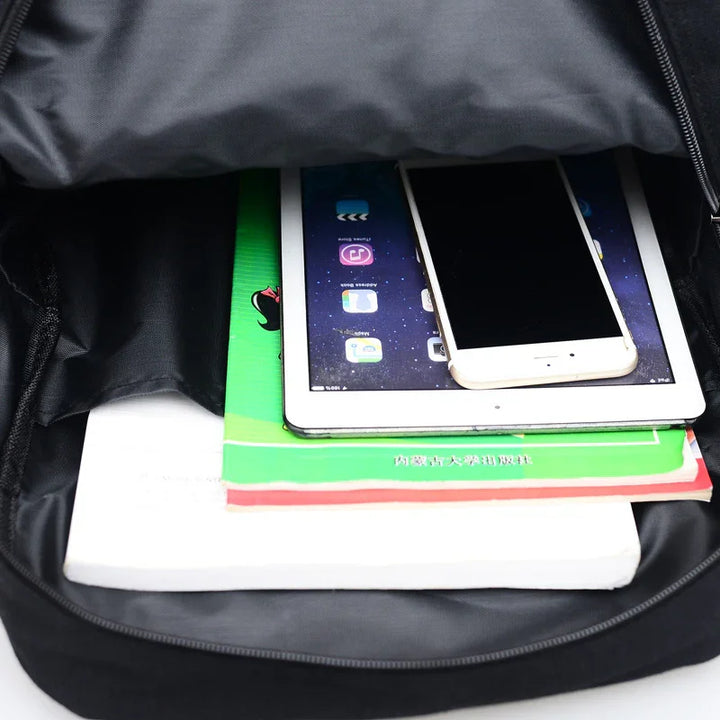 Open black backpack with stacked books, tablet, and smartphone inside on white background